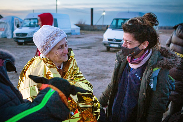 Senior woman in emergency blanket talking to aid worker.