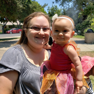 A woman w=poses with a one-year-old baby in a tutu.