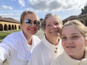 A woman, her mother, and daughter smile outside on a sunny day. 