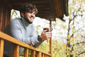 a man sitting on a porch holding a cup of coffee in fall