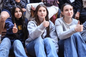 A group of teenage girls sit in a row listening to a presenter and giving a thumbs up sign