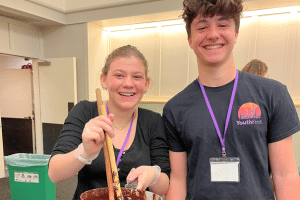 Two teen volunteers mixing a bowl of ingredients and smiling