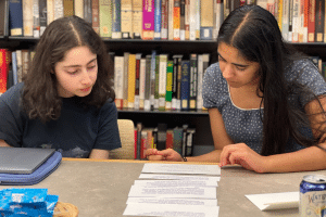 Two teenage girls in a library reviewing a document on a table